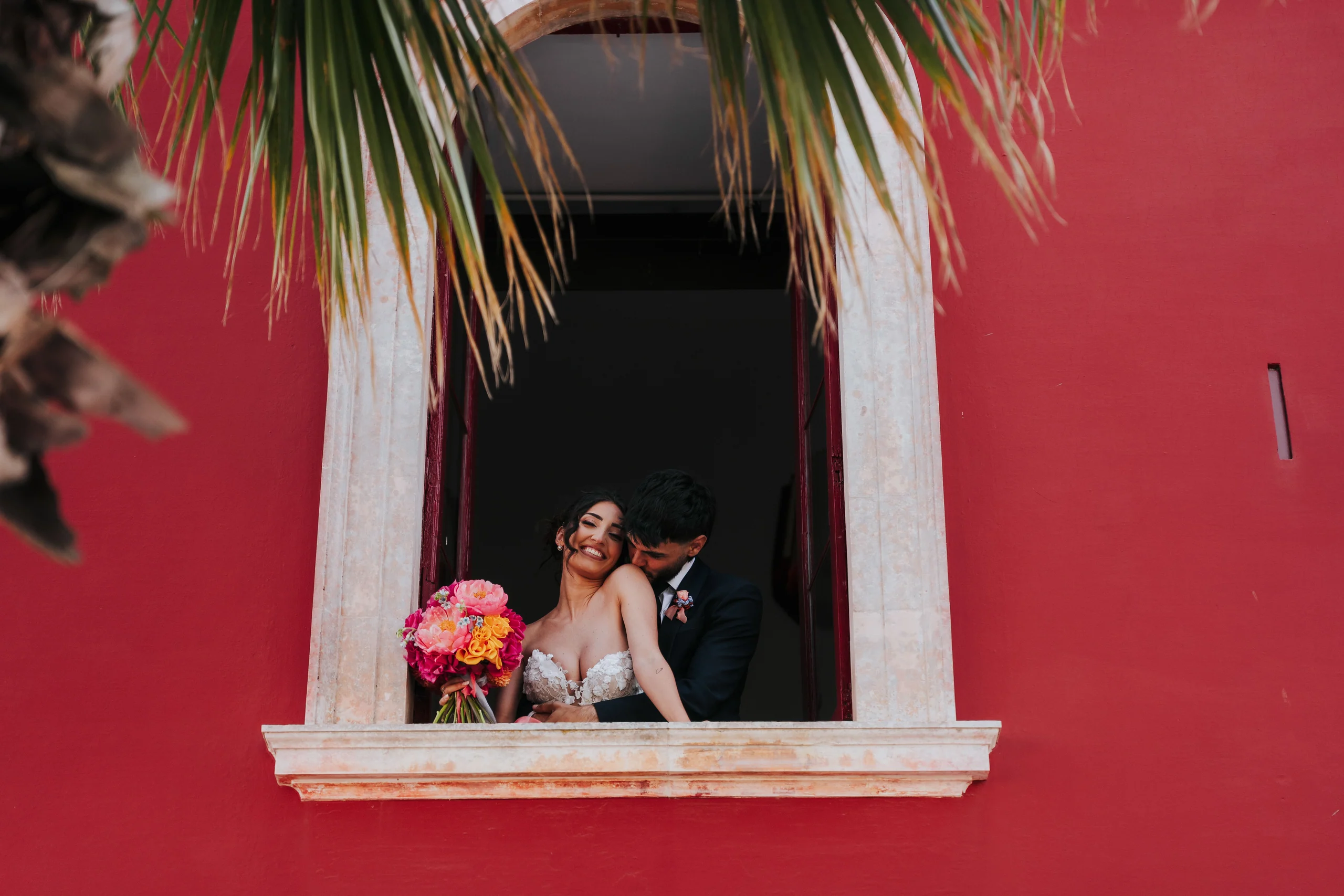 Elenia and Andrea at a window in the red façade of Masseria Mavugliola